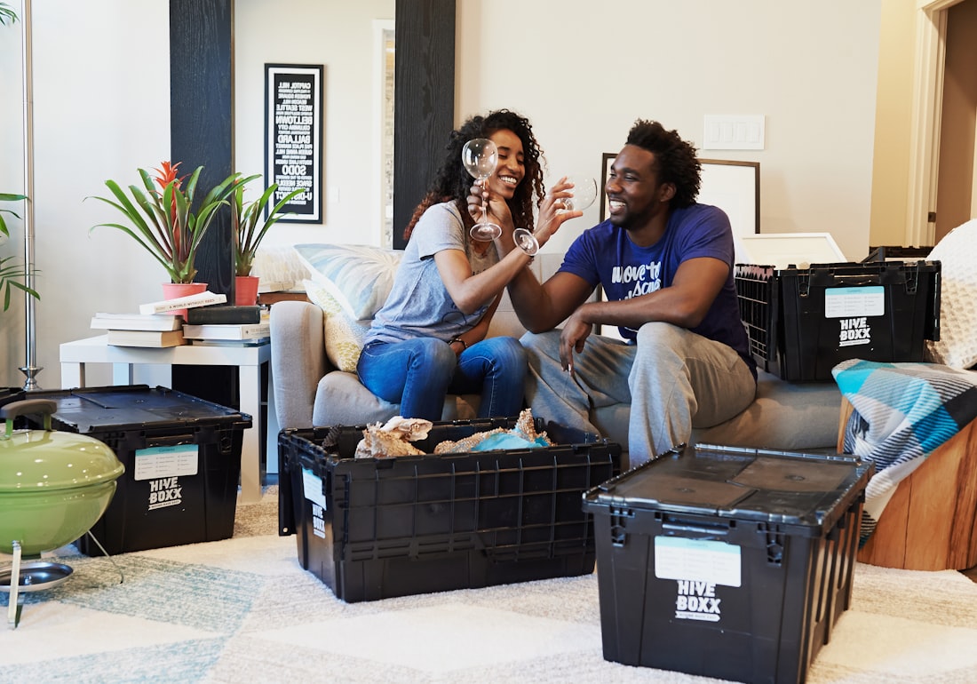 A couple toasting on the couch of their new apartment, moving boxes around them